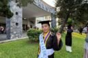 Seorang wisudawati berpose bahagia mengenakan toga lengkap dengan selempang predikat kelulusan 